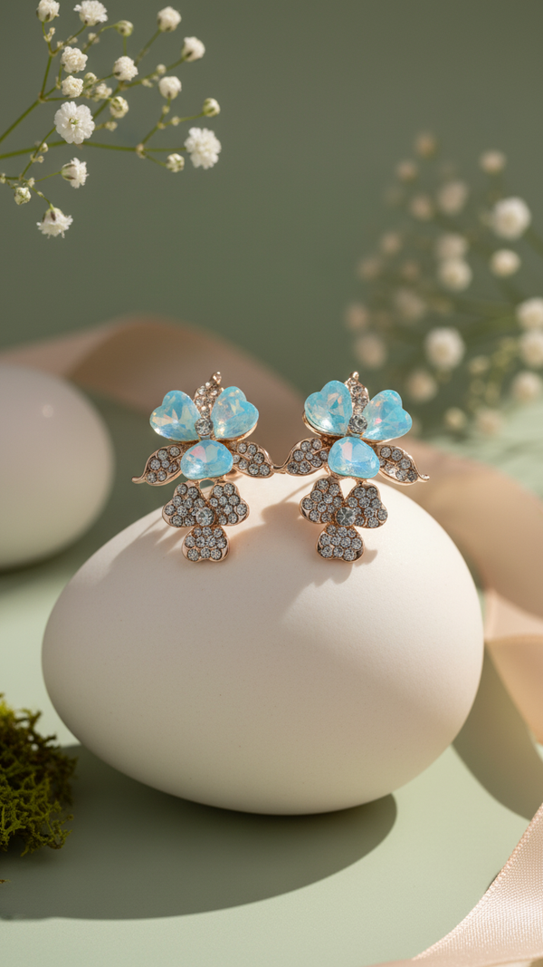 Pair of floral earrings with blue stones on a white surface with a blurred natural background