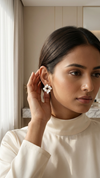 Woman wearing a white turtleneck sweater and geometric earrings indoors.