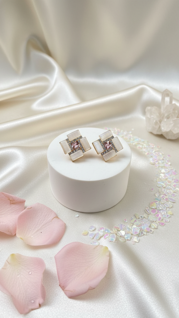Pair of earrings on a white stand with pink petals and glitter on a beige fabric background