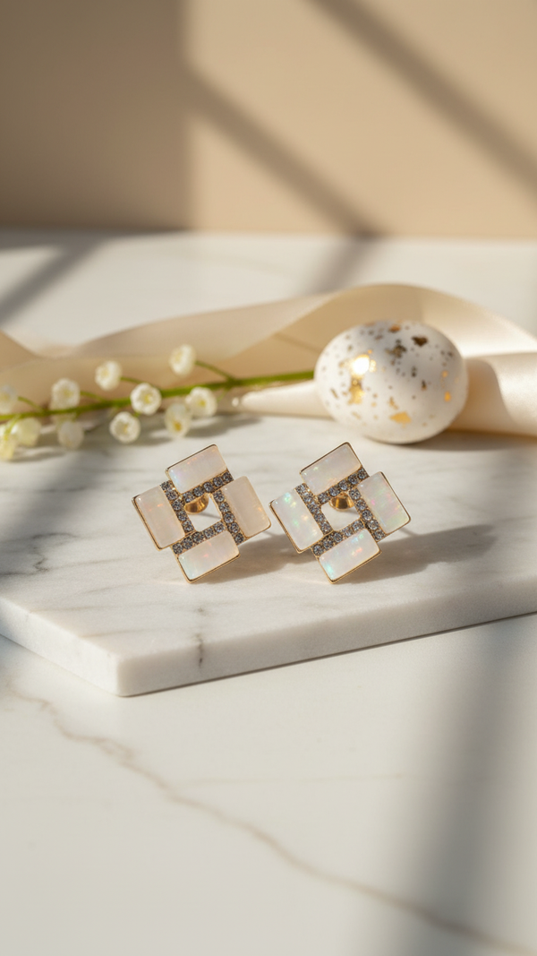 Pair of square earrings with a central gemstone on a marble surface with a soft background.