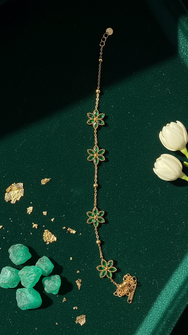 Diaura Jewels minimalist 18K gold plated floral link bracelet featuring marquise-cut emerald green zircons on a woman's wrist.