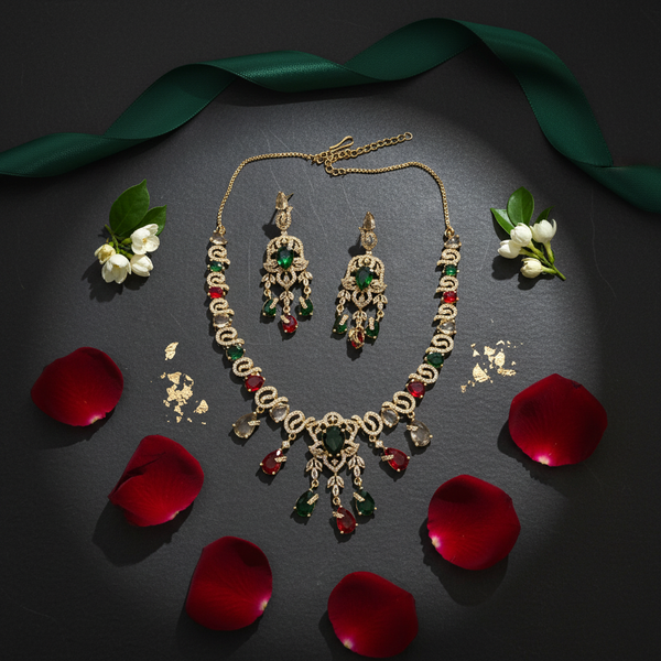 A premium multi-color American Diamond necklace and earring set with emerald and ruby tones, styled on a dark stone background with rose petals and green silk ribbon.
